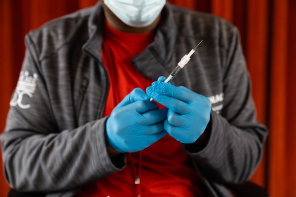 A Black person holds a syringe in their gloved hands.