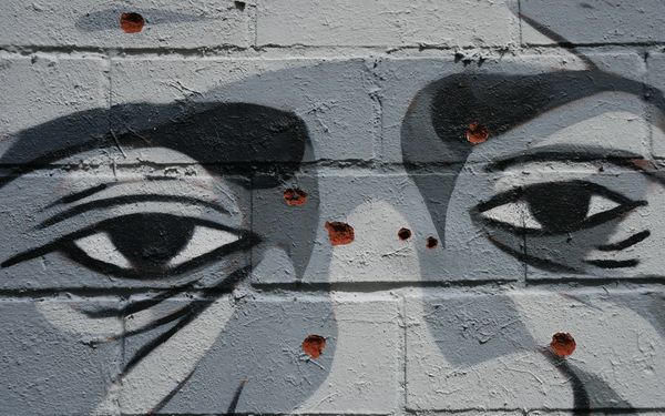 A gray mural with a Black man's eyes is shown. There are red spots on the mural that make it look like someone has tried to destroy it.