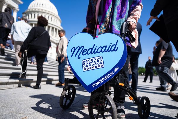 A blue sign shaped like a heart that says "Medicaid" hangs from a person's walker outside the U.S. Capitol building. 