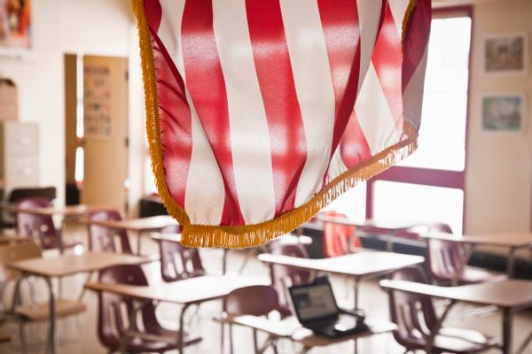An American flag, with red and white stripes, hangs in front of an empty classroom. 