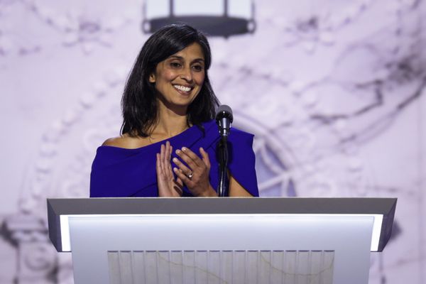 An Indian woman wearing a blue dress stands behind a podium.