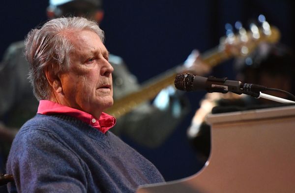 A white man sits at a piano with a microphone attached.