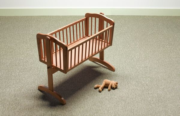 An empty crib with a teddy bear beside it. 