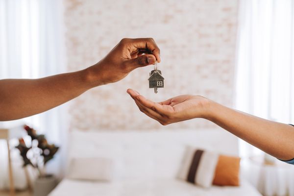 One person hands another person a set of keys with a house charm on them. 