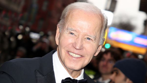 A white man wearing a black suit and bowtie smiles while looking at the camera.