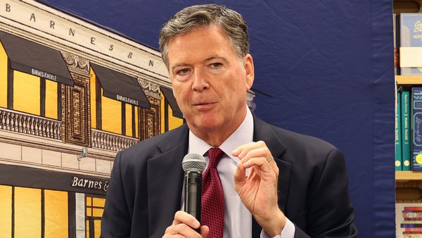 A white man in a suit speaks while holding a microphone. 