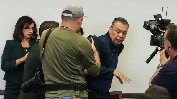 Several people surround a Latino wearing a dark blue jacket. Two of the people appear to hold cameras.