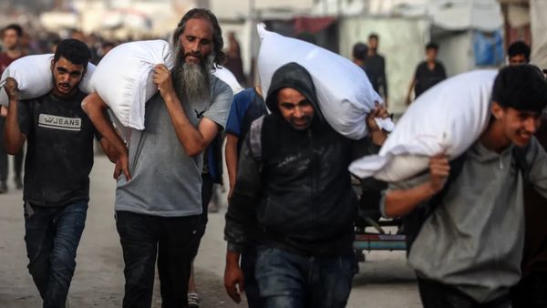 Four Palestinian men carrying flour on their shoulders. 