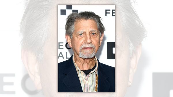 A white man being photographed looks at the camera.