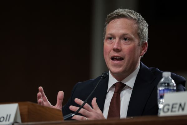 A white man speaks behind a microphone while sitting down.