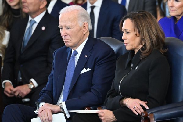 Former U.S. President Joe Biden, a white man in a suit with white receding hair, sits beside former Vice President Kamala Harris, an Asian and Black woman with brown hair in a black jacket. 