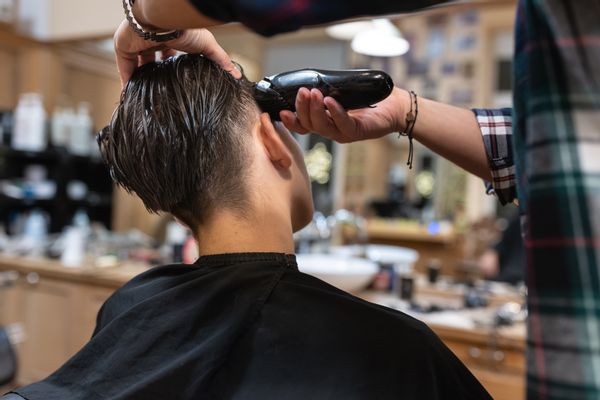 A hairdresser cuts a teenager's hair and gives him a modern haircut in an old-fashioned, retro-decorated hair salon.