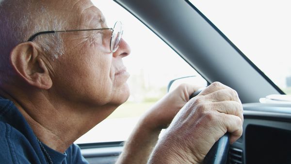 A white person wearing glasses grips the wheel of the car they are driving.