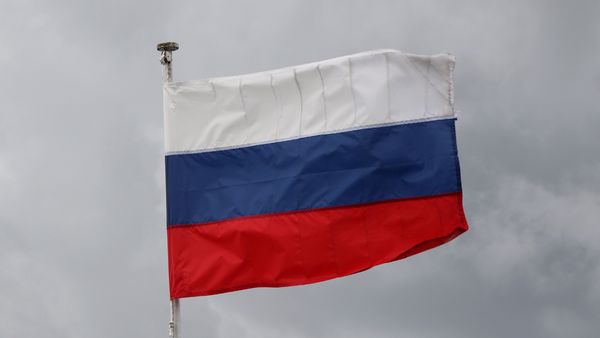 A flag with three horizontal stripes—white on top, blue in the middle, and red on the bottom—waving on a flagpole against a cloudy gray sky. This is the national flag of Russia.