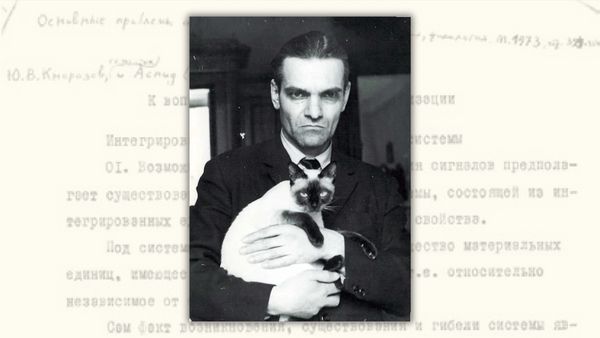 In the foreground: A black and white headshot photo of a stern man holding what appears to be a Siamese cat. In the background: Russian text. 