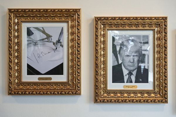 Two black and white portraits in gold frames. The portrait on the left is labeled "Joseph R. Biden" and shows a photo of a machine signing Biden's name. The portrait on the right is a headshot of U.S. President Donald Trump. 
