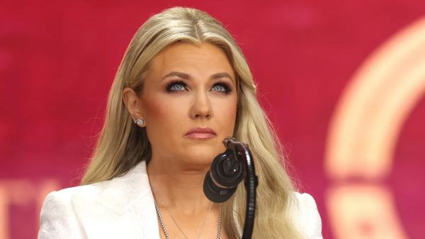 A white woman looks upwards while sitting down. A microphone is in front of her.