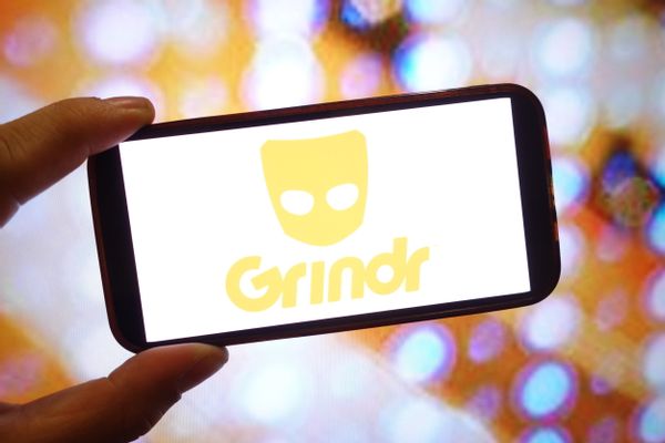 A hand holds up a phone with a yellow "Grindr" logo on it. 