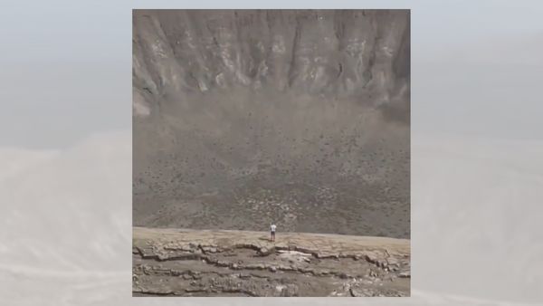 A person stands in front of a huge crater.