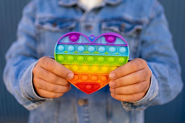 A man holds up a rainbow sensory push pop toy shaped like a heart.