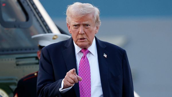 U.S. President Donald Trump, a tan white older man in a suit, points at the camera. 