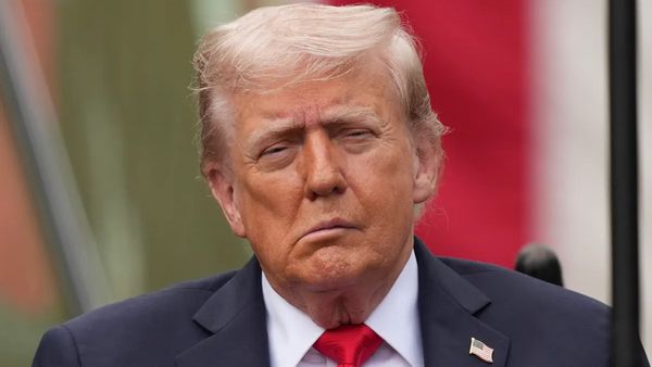 A white man wearing a blue suit faces the camera. The left side of his face appears to droop.