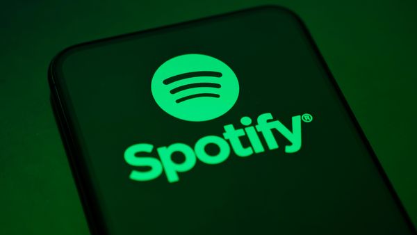 "Spotify" in green text and a green Spotify logo appear on a smartphone reflecting a green light. 
