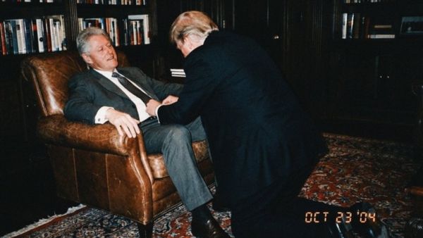 A white man wearing a suit appears to be kneeling and grabbing at the jeans of another white man.