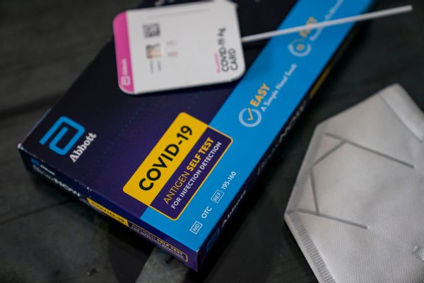An Abbott COVID-19 self test is shown, with test results shown on top of the box. To the right, a white mask is shown.