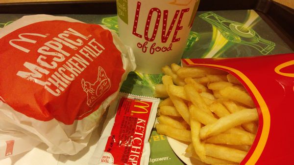A McSPICY CHICKEN FILLET, French fry and drink that says LOVE of food is shown on a tray. A ketchup packet is seen between the sandwich and fry.