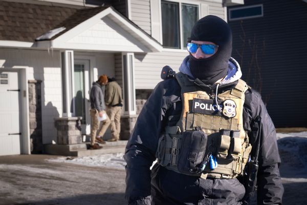 A masked ICE officer outside of a house in the snow.