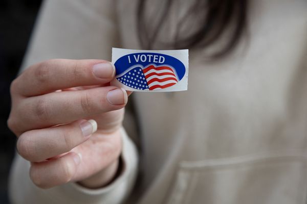 A person affixes an "I voted" sticker to their sweatshirt. 