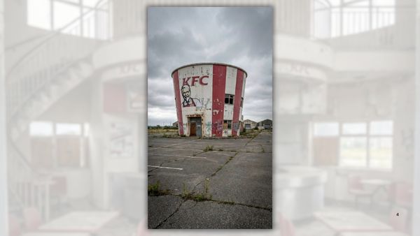 An AI-generated image of a KFC restaurant shaped like one of its buckets taken from the outside. It sits abandoned in an empty parking lot with little in the background. Windows are broken and/or partially boarded up.