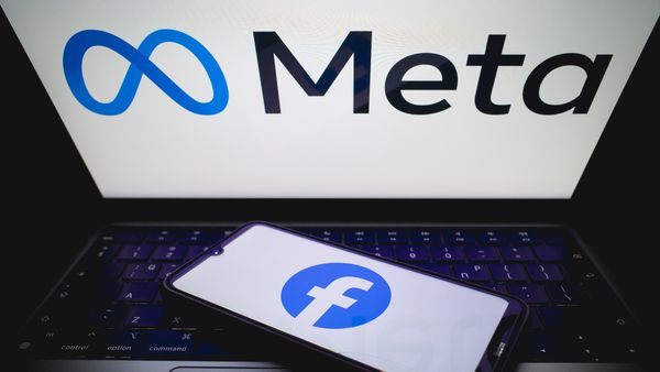 "Meta" logo appears on a laptop screen while a smartphone with the "Facebook" logo rests on the keyboard