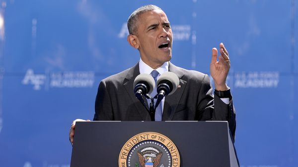 President Barack Obama is shown in 2016 wearing a suit with a blue patterned tie and standing in front of a podium with the U.S. presidential seal.