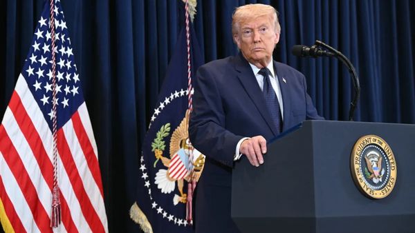 President Donald Trump, a white man wearing a dark blue suit, stands at a podium.