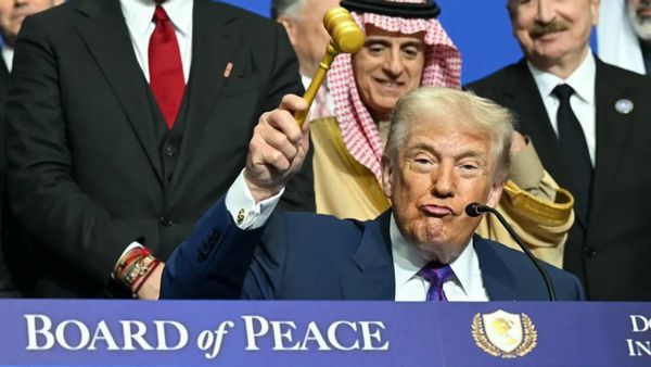 U.S. President Donald Trump, seated, purses his lips and bangs a golden gavel. Foreign dignitaries stand behind him, watching. In front of him, a sign reads "Board of Peace."