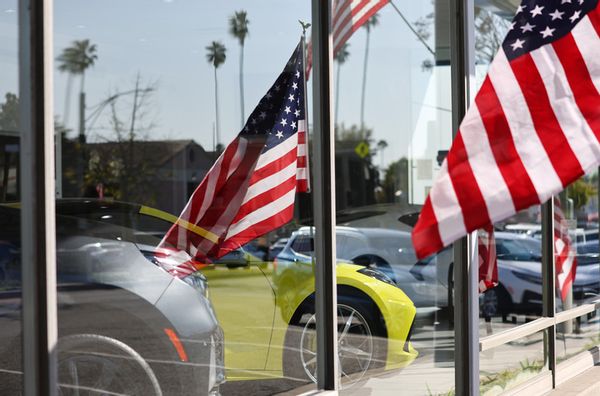 A U.S. flag is mirrored in the window of a car dealership selling new cars. 