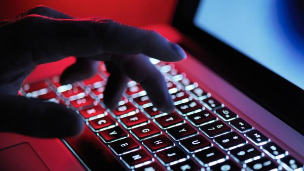 A photo shows a hand with a red light behind it typing on a laptop in a close-up shot.