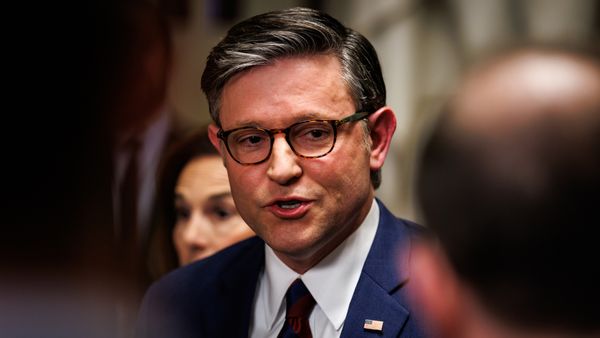 Close up photo portrait of Mike Johnson, a white man wearing glasses and a blue suit, talking to out-of-focus people in the foreground