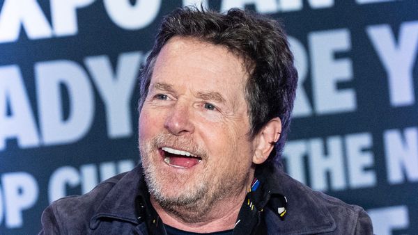 Actor Michael J. Fox, a white man, is pictured smiling in front of a background featuring various words.