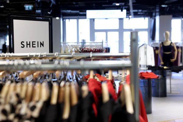 Racks of clothing are shown inside a store. In the corner, SHEIN can be seen on a screen.