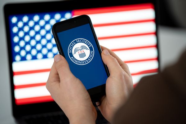 Image shows a hand holding a cell phone that reveals the Social Security Administration logo.