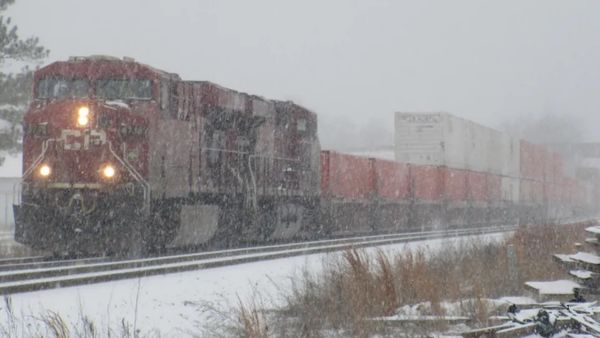 A red freight train moving along the tracks in snowy weather