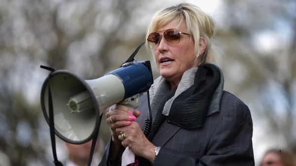 A white woman is shown speaking into a megaphone.
