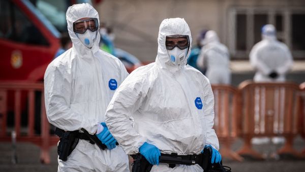 Two people in full personal protective equipment, including white jumpsuits, masks, gloves and goggles.