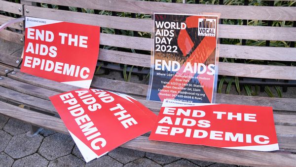 Red posters that say, "END THE AIDS EPIDEMIC" scattered on a bench. 