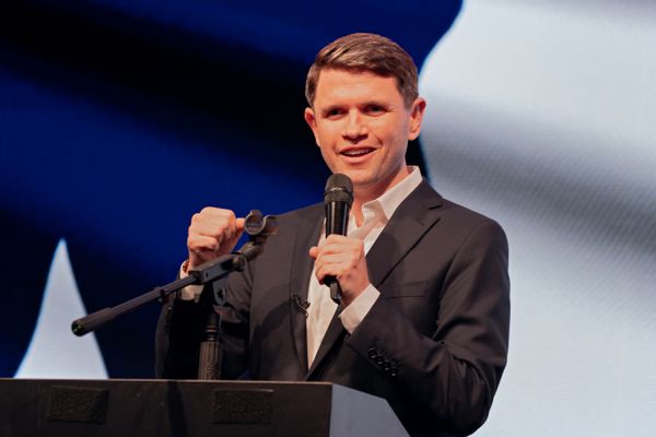 James Talarico, a young white man with short, well maintained hair, wearing a suit, talking at a podium while holding a microphone.