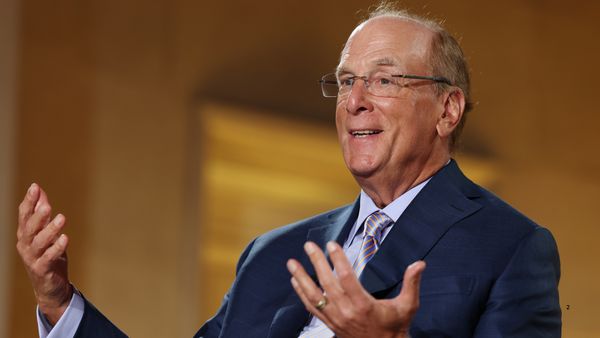 An older white man — Larry Fink — wearing a suit, sitting in a chair and gesturing with his hands while talking.