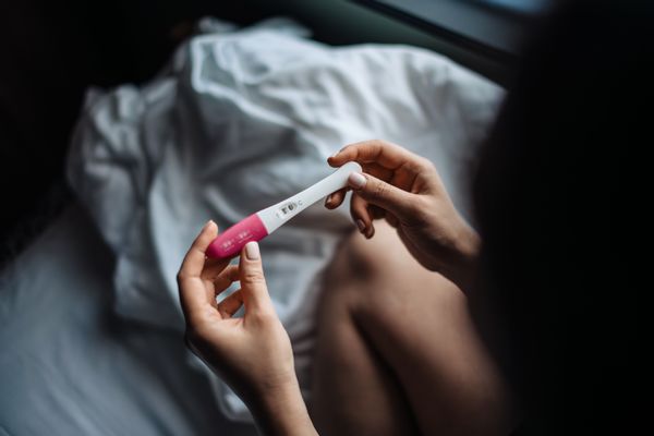 A person holds up a pregnancy test in a bedroom. 